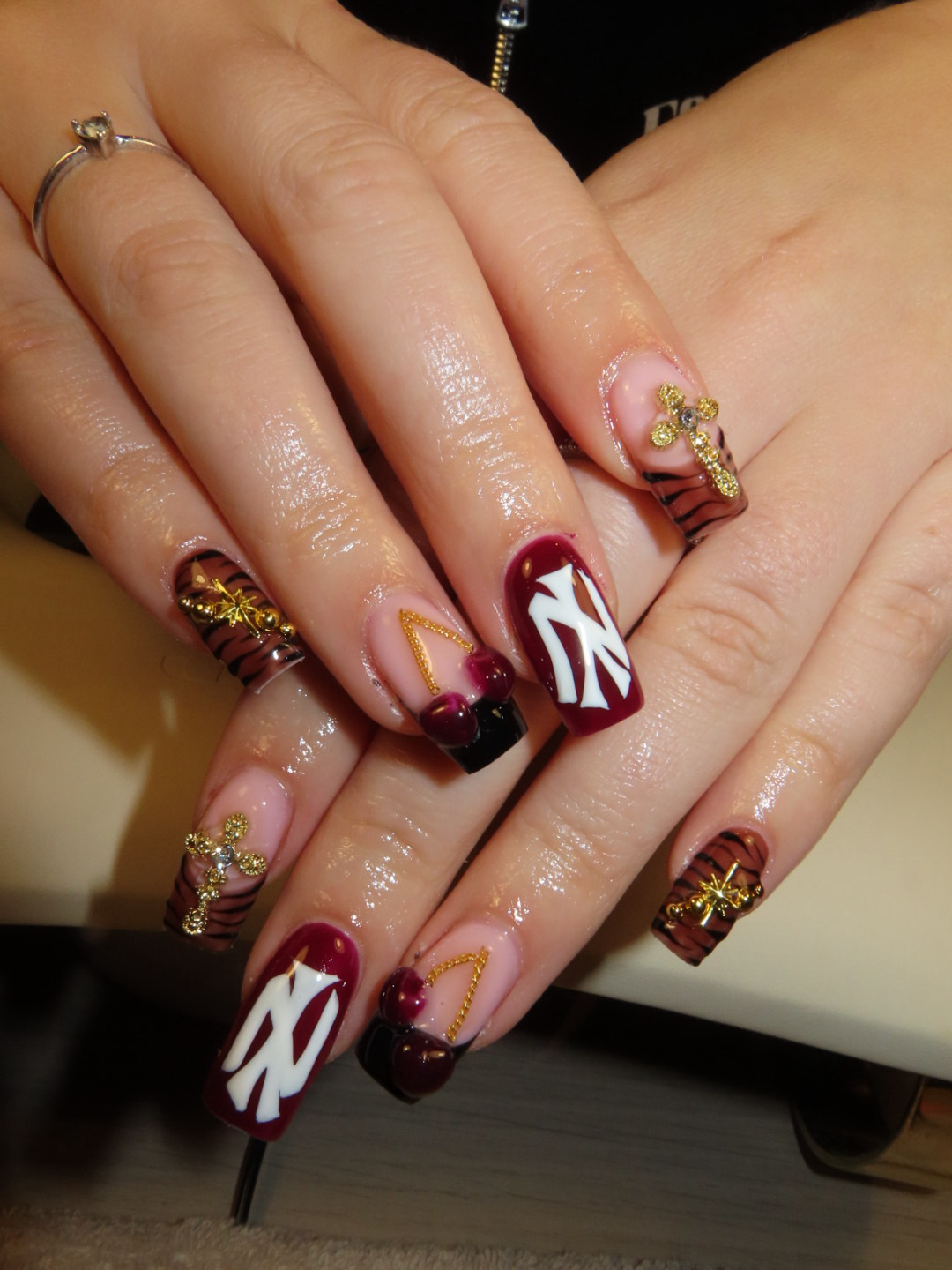 Bordeaux nagels met een wit NY-logo, gouden bedels en tijgerstrepen