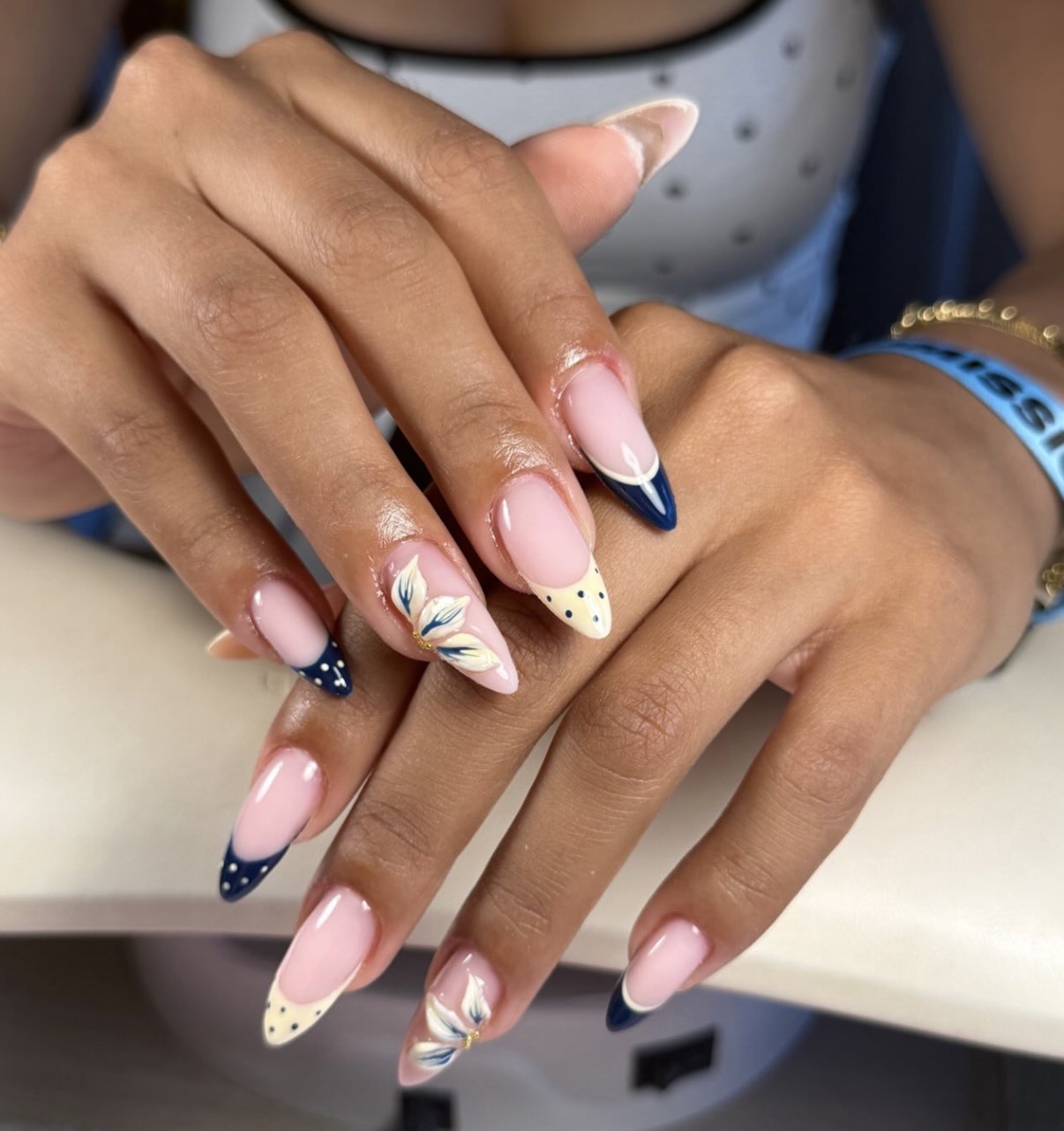 Lange amandelnagels in nude met een marineblauwe french, stipjes en een geschilderd bloemetje