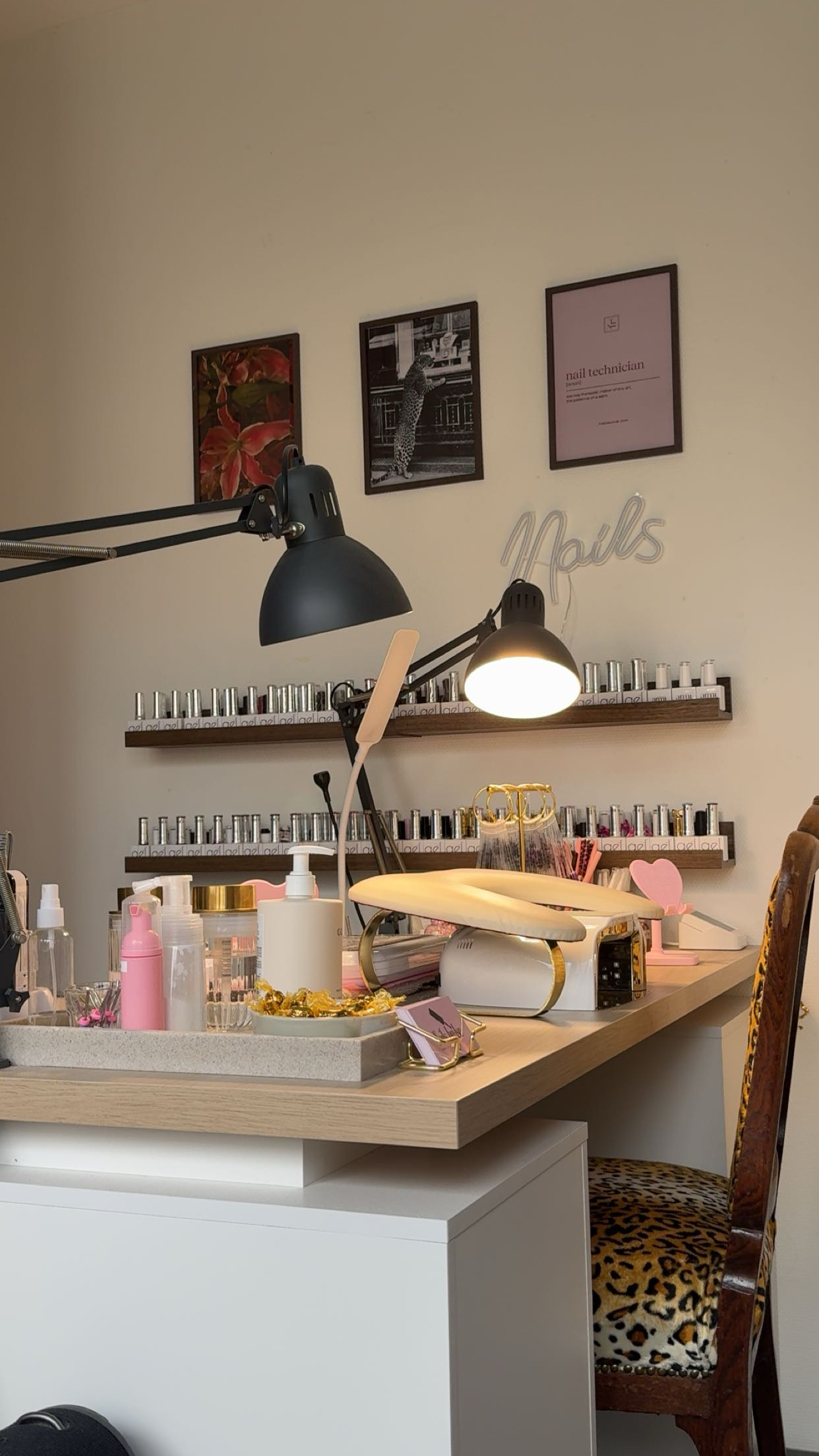 De studio van Nails by Ise: een tafel met lampen, een neonbord met Nails, lijstjes aan de muur en planken vol gelflesjes